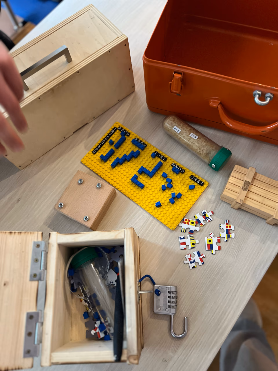 Rätselstation von „Die Bombe“: Holzboxen, Zahlenschlösser und Code-Tafeln auf einem Tisch